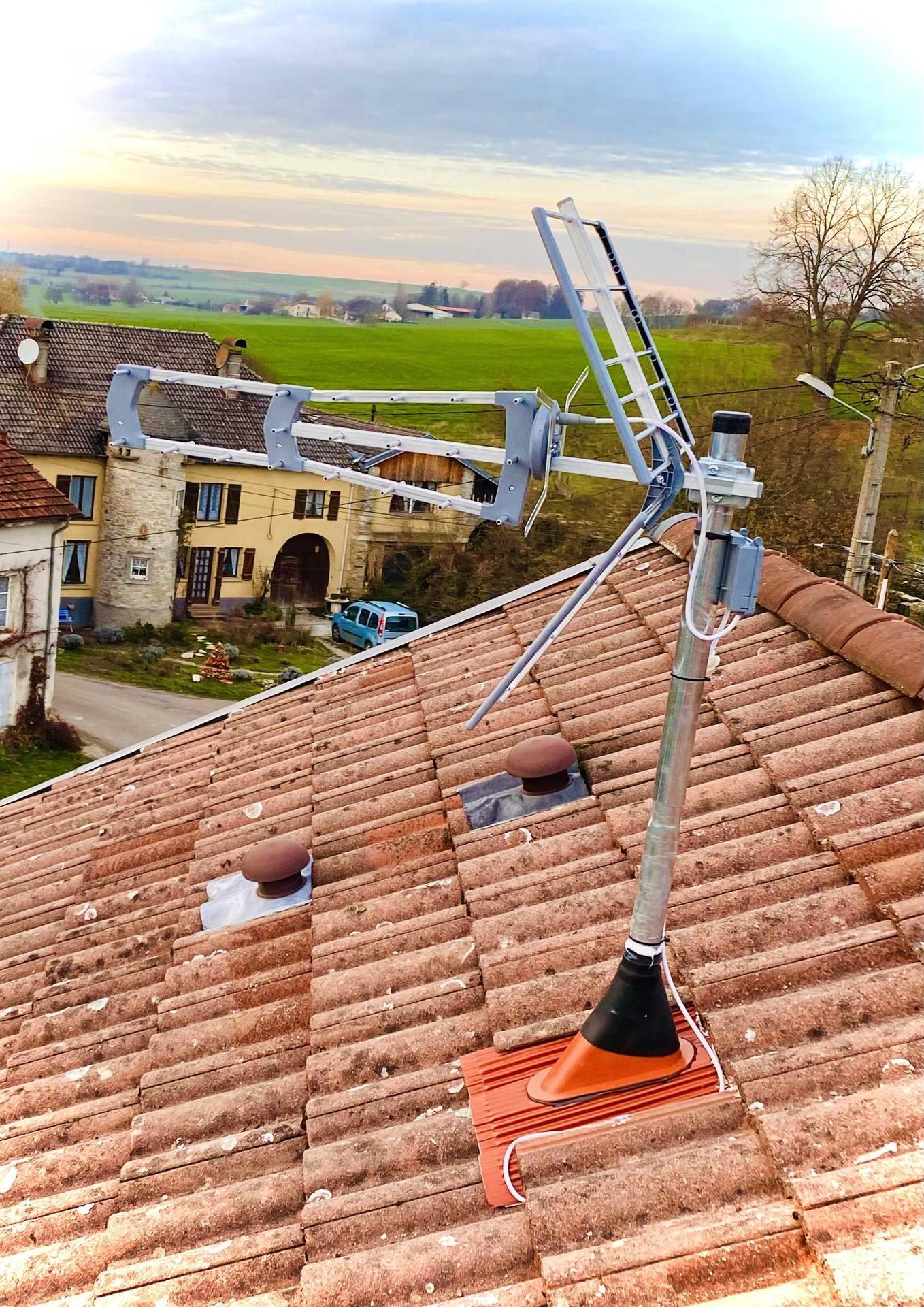 Antenne TV posée sur un toit de tuiles, campagne vosgienne au coucher du soleil